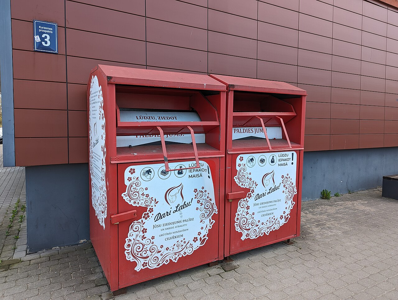 Two red textile collection boxes beside a building in Riga.