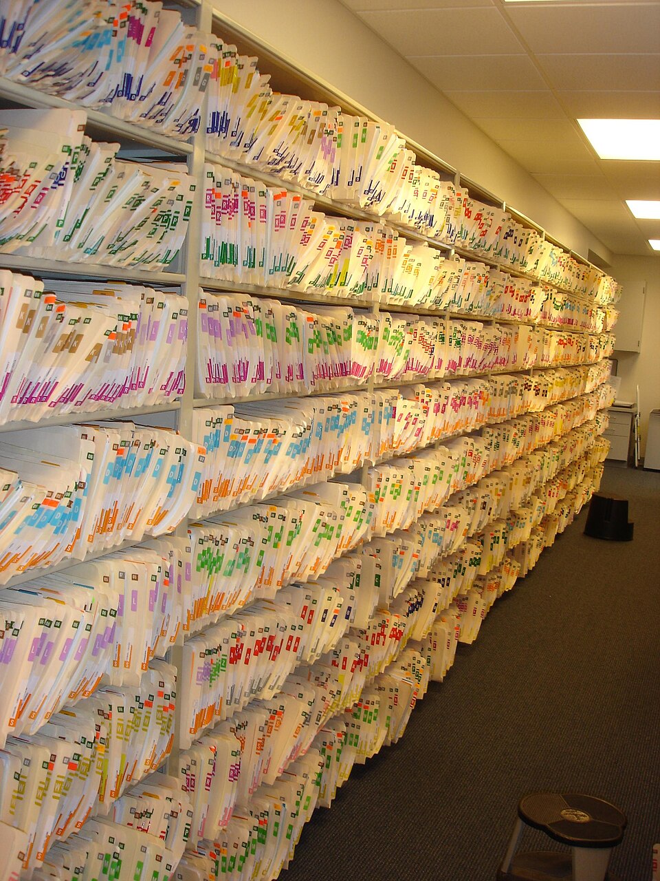Rows of color-coded folders fill open shelves in an office records room.